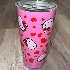 a pink hello kitty tumbler cup with hearts and bows on the lid is sitting on a wooden surface