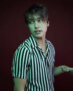 a man with green paint on his face and hands in front of him, wearing a striped shirt