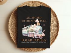 a black t - shirt with an image of a train on the front and words all aboard to the north pole polar express