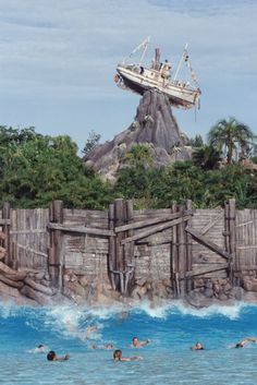 people are swimming in the water near an amusement park with a pirate ship on top