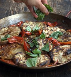 a pan filled with grilled vegetables on top of a wooden table next to a person's hand