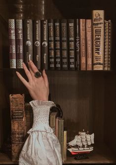 a hand reaching out from behind a book shelf with books on it and a ship in the background