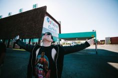 a man standing in front of a building holding his arms up to the sky while wearing sunglasses