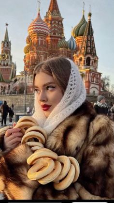 a woman wearing a fur coat and scarf holding bananas in front of an ornate building