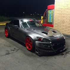 a gray car parked in front of a gas station at night with red rims