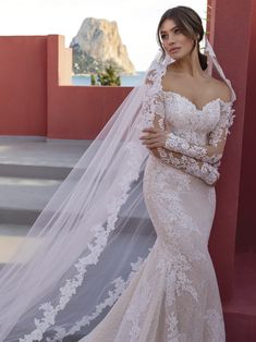 a woman wearing a wedding dress with a veil on her head standing in front of a red wall