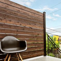 a black chair sitting on top of a cement floor next to a wooden slatted wall