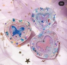 three heart shaped brooches with butterflies and stars in them on a purple background