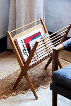 a wooden magazine rack sitting on top of a rug next to a chair and window