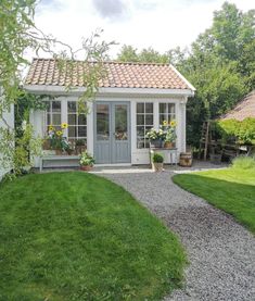 a small white shed sitting in the middle of a lush green yard next to a gravel path