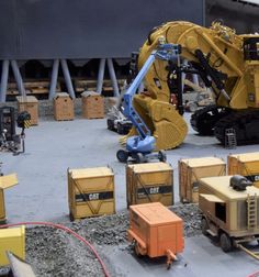 construction equipment is displayed on the ground in front of other vehicles and boxes, including an excavator