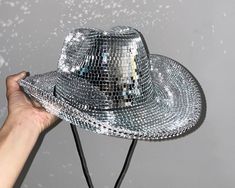 a person's hand holding up a shiny silver hat that is falling into the air