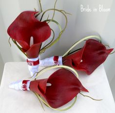 two red flowers are sitting on top of a white table with the stems wrapped around them