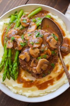 a white plate topped with mashed potatoes covered in mushrooms and gravy next to asparagus