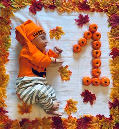 a baby laying on top of a blanket covered in leaves and pumpkins next to the letter h