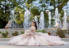 a woman in a wedding dress sitting on the ground next to a fountain with water spouting from it