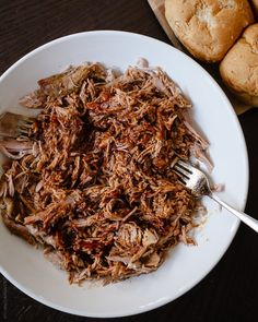 a white plate topped with shredded meat next to rolls