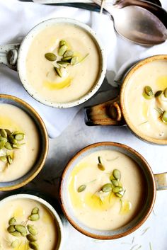 four bowls filled with soup sitting on top of a white table cloth next to spoons