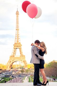 a man and woman kissing in front of the eiffel tower with two balloons