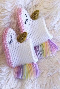 two crocheted unicorn mittens laying on top of a white rug with fringes