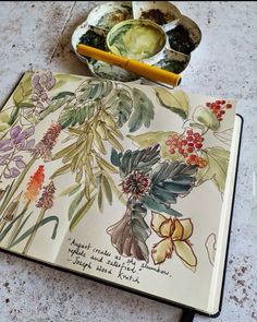 an open notebook sitting on top of a table next to a bowl of fruit and saucers