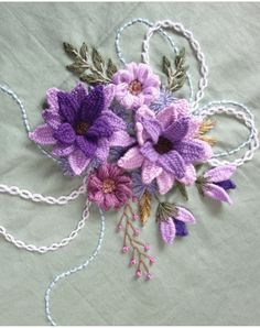 crocheted flowers and leaves are displayed on a tablecloth with white thread in the middle