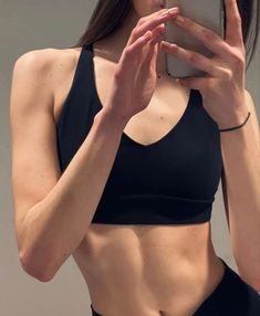 a woman in black sports bra holding up her cell phone to her face and looking at it