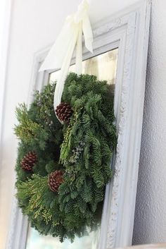 a wreath hanging on the wall with pine cones and evergreens in front of it