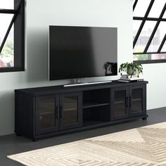 a large flat screen tv sitting on top of a black entertainment center next to a window