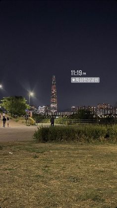 people are walking around in the park at night with city lights and buildings behind them