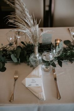 the table is set with silverware and greenery