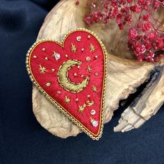 a heart shaped brooch sitting on top of a piece of wood next to flowers