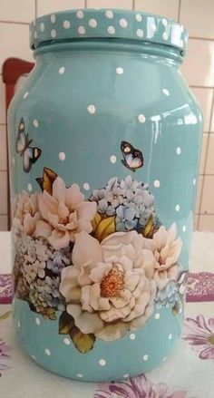 a blue jar with flowers painted on it sitting on a table next to a tiled wall