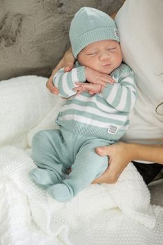 a woman holding a sleeping baby on top of a white blanket and wearing a blue hat