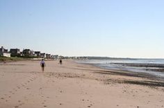 two people walking on the beach with houses in the background