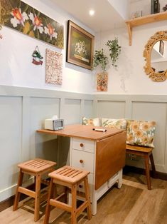 a room with two stools, a table and pictures on the wall above it