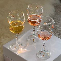 three wine glasses sitting on top of a white box filled with different colored liquids