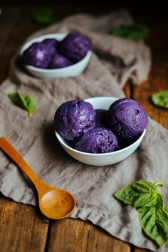 two bowls filled with purple ice cream sitting on top of a wooden table next to leaves