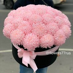 a pink flower arrangement in a black box on the street with a ribbon around it