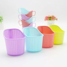 four different colored cups sitting next to each other on a white surface with flowers in the background