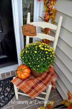 a white rocking chair with flowers and pumpkins on the front porch for fall decor