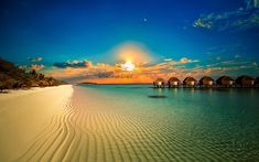 the sun is setting over an island with thatched huts in the water and sand on the beach