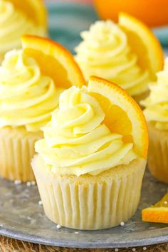 cupcakes with frosting and orange slices on a metal plate next to an orange slice