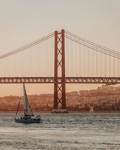 a sailboat in the water near a large bridge with a city in the background