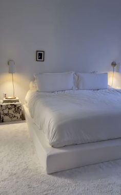 a large white bed sitting in a bedroom next to two nightstands with lamps on them