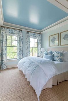 a bedroom with blue and white walls, carpeted flooring and two large windows