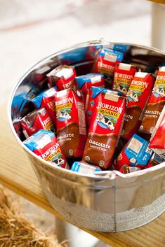 a metal bucket filled with chocolates on top of a wooden table next to hay