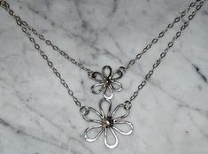 "Delightful Sterling Daisies hand forged from recycled silver are suspended on an 18\" sterling 2 layered chain. The silver petals are hammered for texture and then polished for a high sheen. Large daisy measures 1 1/4\" x 1 1/4\" (30cm x 30cm) and small daisy measures 1\" x 1\" (24 x 24cm). You may choose single small daisy, single large daisy, or the double daisy necklace." Hand Forged Silver Dainty Necklace, Silver Flower Pendant Necklace With Soldered Detail, Large Daisy, Layered Chain, Daisy Necklace, Recycled Silver, Multi Strand Necklace, Nashville Tn, Strand Necklace