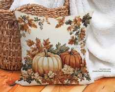 a decorative pillow with pumpkins and flowers on it next to a wicker basket