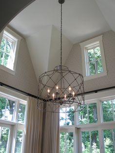 a chandelier hanging from the ceiling in a room with large windows and curtains